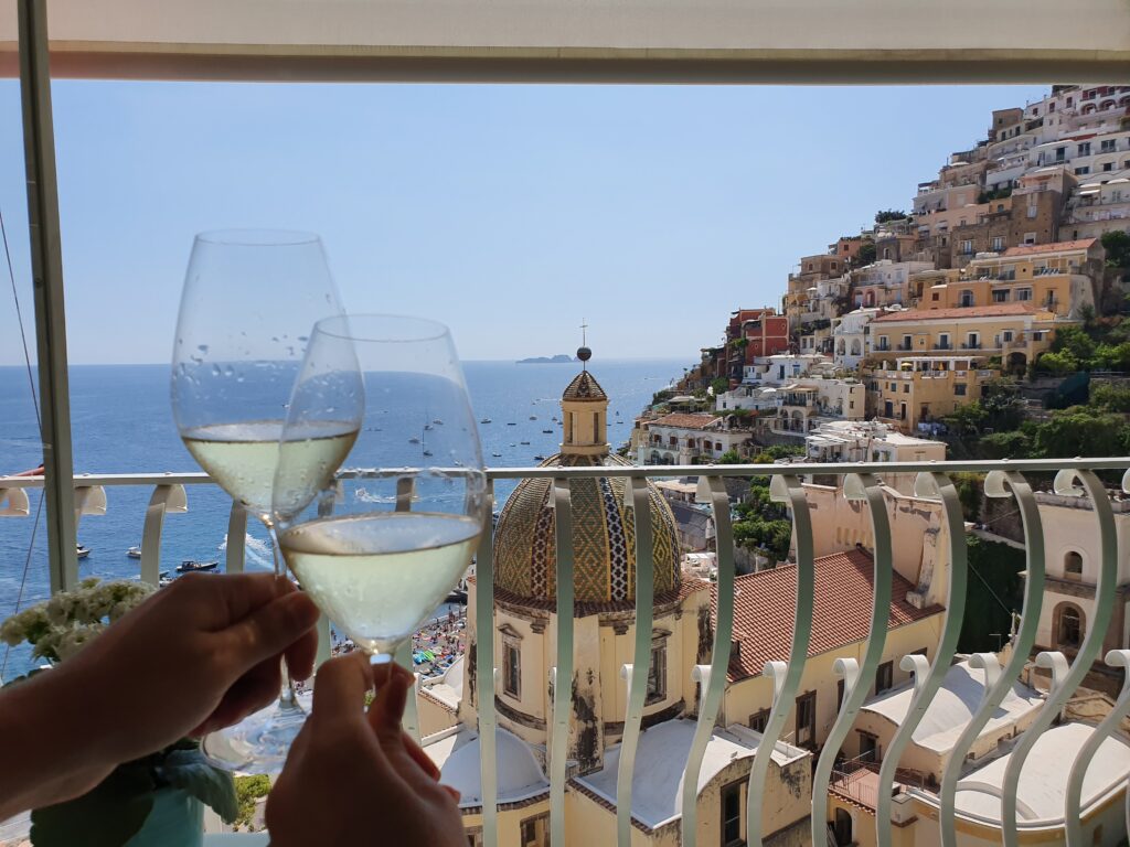 Couple in Amalfi drinking wine on a balcony overlooking the town and sea. Romantic getaway. Allegro Luxury Vacations, Brenda Ajay, travel specialist.