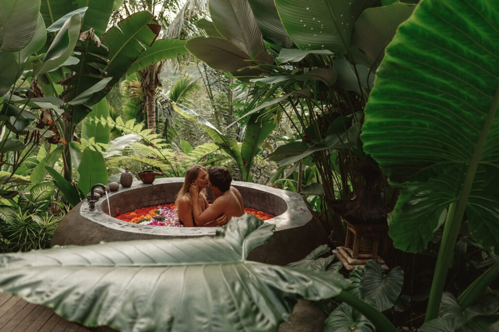 Beautiful couple resting in hotel spa. Woman and man relaxing in bath with tropical flowers outdoor at luxury hotel resort in the jungle. Romantic getaway. Honeymoon in Bali.  Allegro Luxury Vacations. Brenda Ajay, Virtuoso luxury travel advisor.