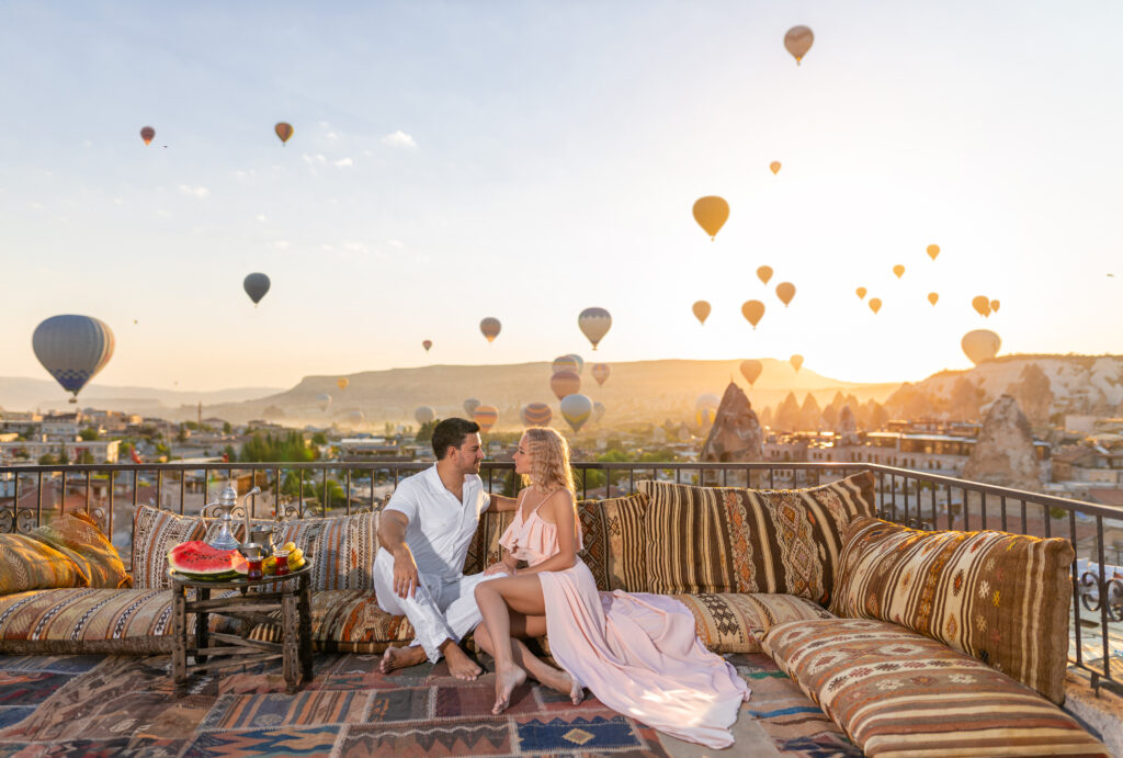 Beautiful morning in Cappadocia - a young couple and their romantic breakfast with amazing background of flying balloons. Romantic getaway. Allegro Luxury Vacations, Brenda Ajay, travel specialisst.