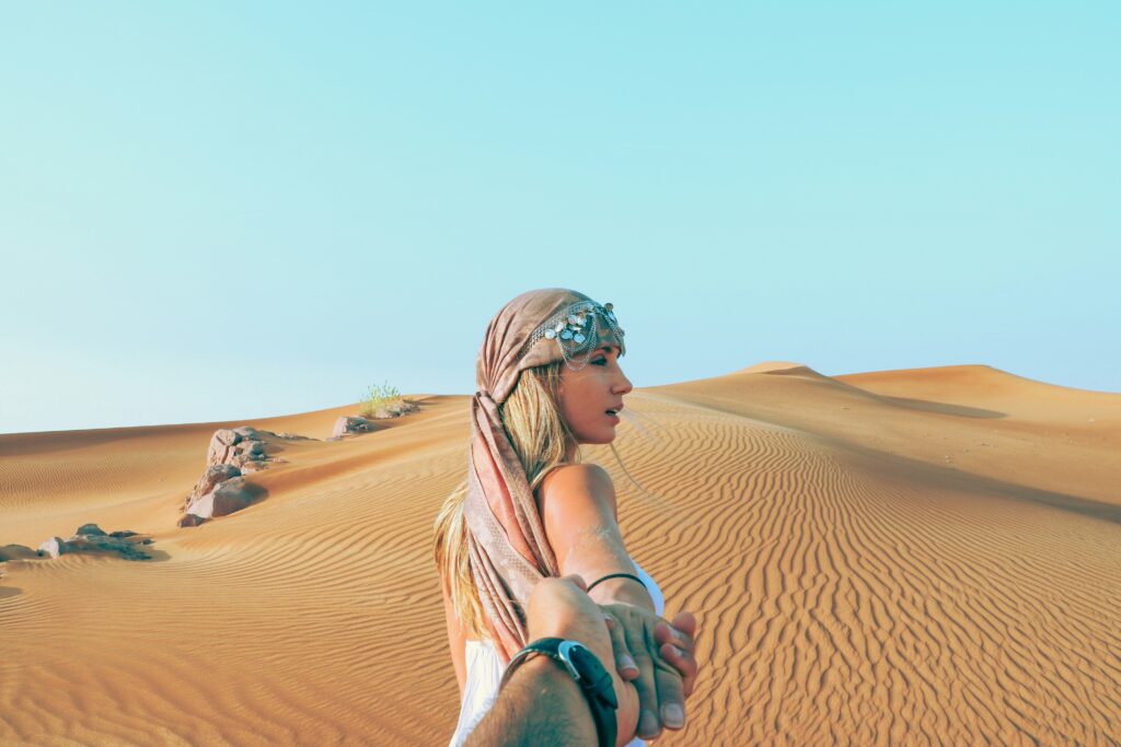 A romantic couple hold hands as they walk through the desert outside of Dubai. Romantic exotic getaway. Allegro Luxury Vacations, Brenda Ajay Virtuoso luxury travel advisor