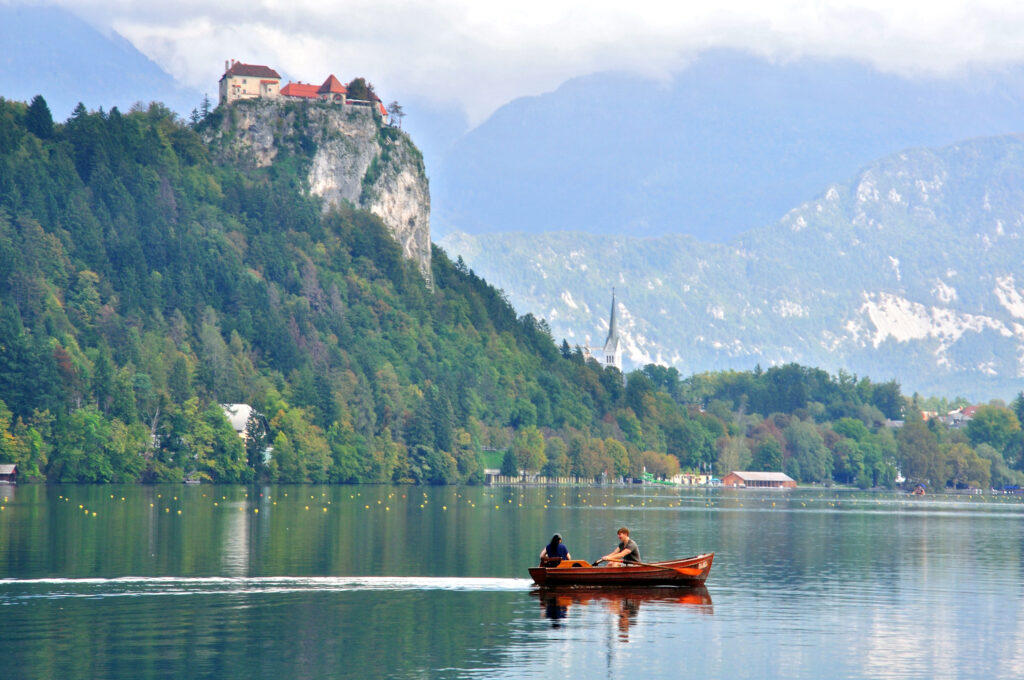 A romantic couple sail in a boat on Bled lake. Bled is a town on Lake Bled in the Upper Carniolan region, Slovenia. Romantic getaway. Allegro Luxury Vacations. Brenda Ajay, Virtuoso luxury travel advisor.