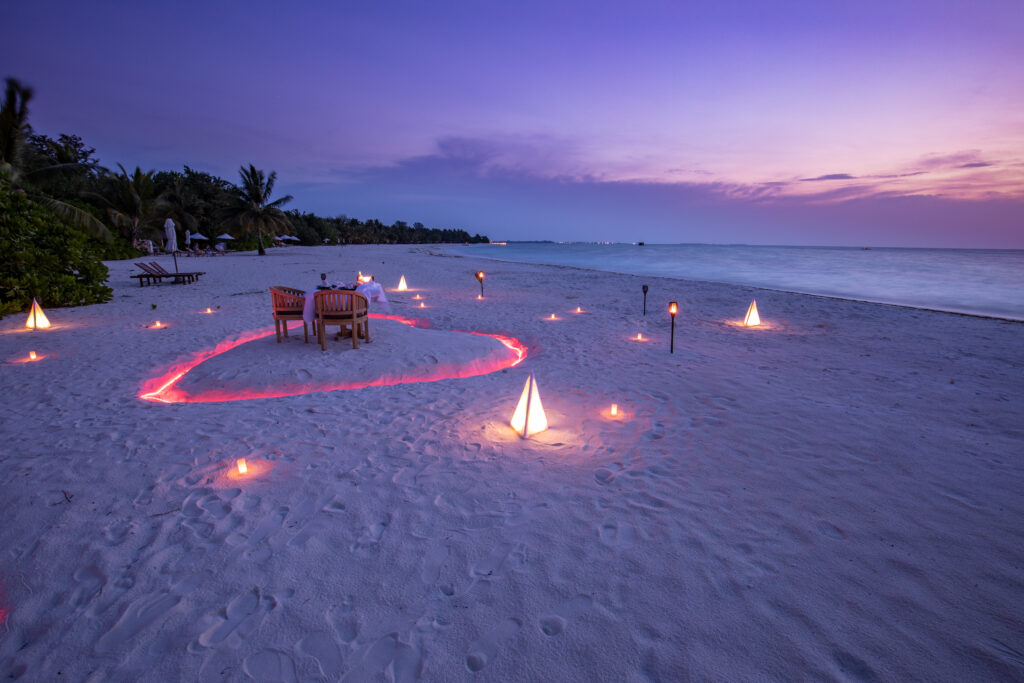 A private romantic candlelit beach setting at sunset awaits a couple in love. Romantic getaway. Allegro Luxury Vacations. Brenda Ajay, Virtuoso luxury travel advisor.