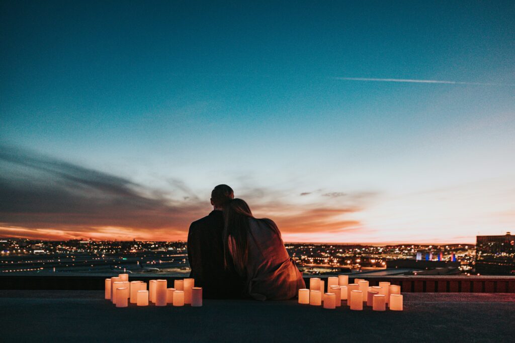 Couple sitting on a rooftop overlooking a city skyline by candlelight at sunset. Romantic getaway. Allegro Luxury Vacations, Brenda Ajay, travel specialist.