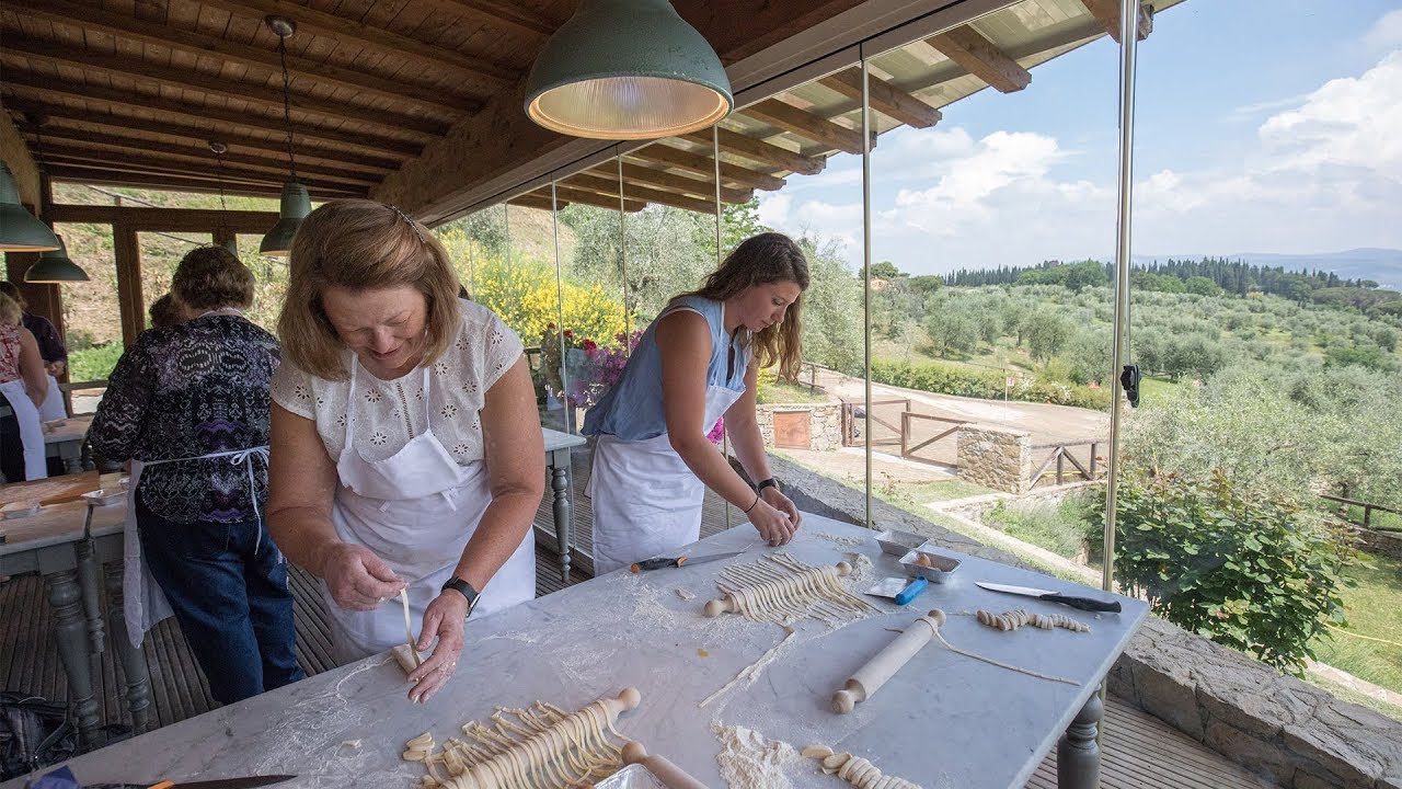 First trip to Italy tips, plan early and reservations are a must. Travelers learning to make fresh pasta during a cooking class in Tuscany with views of the Italian countryside